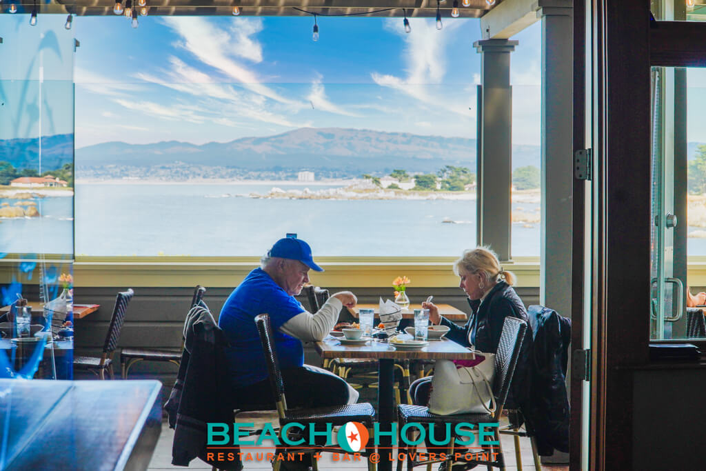 This is an image of a couple sitting at a table across from each other on the outdoor patio with an ocean view at The Beach House Restaurant at Lovers Point in Pacific Grove, California