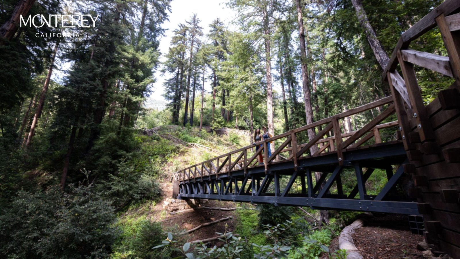 This is an image of two women standing on a wooden bridge looking out across a scene of big redwood trees. They are on the Pfeiffer Falls Trail at Pfeiffer Big Sur State Park