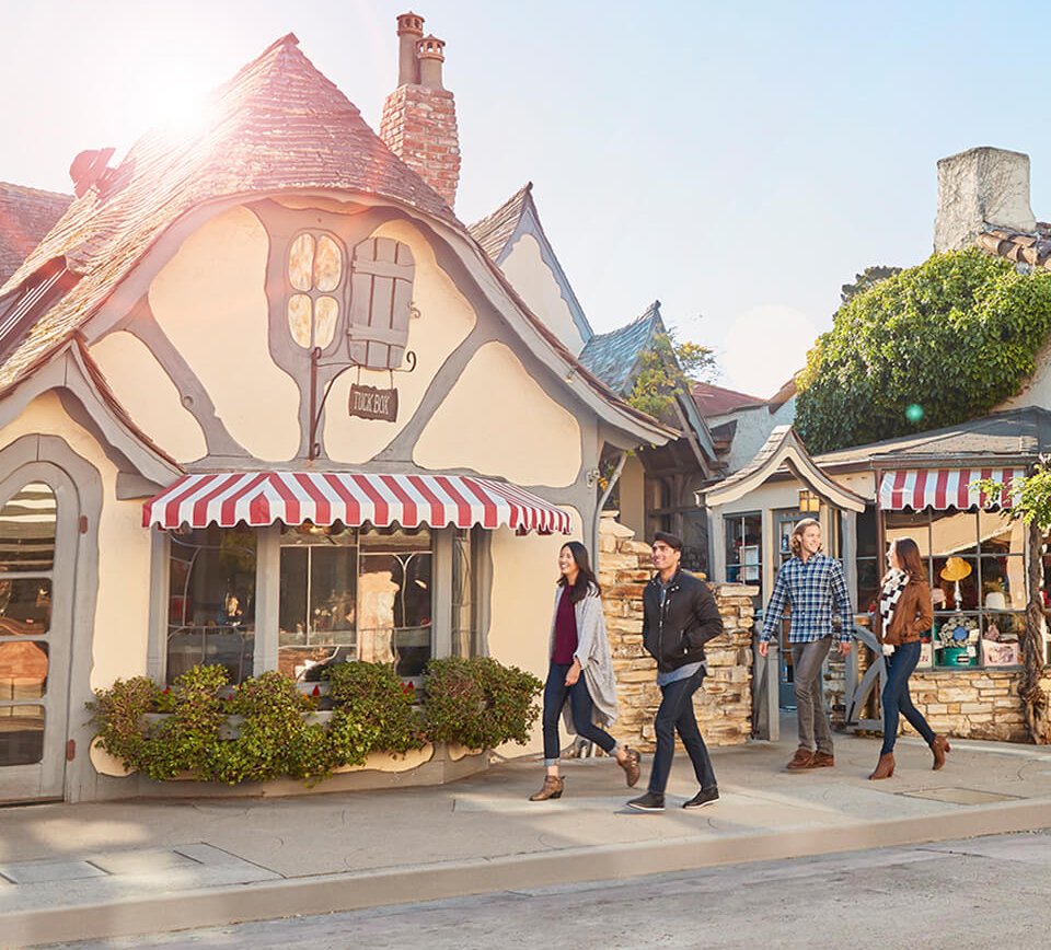 This is an image of a group of people walking on a sidewalk in front of a cottage-like shop in Carmel-by-the-Sea