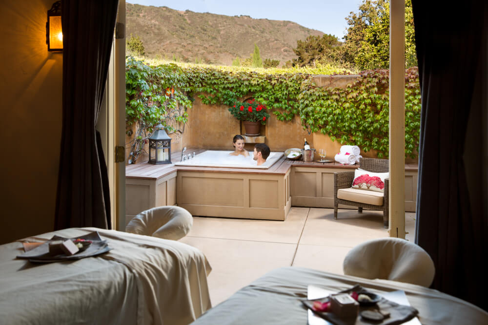 This is an image of a couple sitting in a jacuzzi in the background of two massage tables at Bernardus Lodge & Spa in Carmel Valley