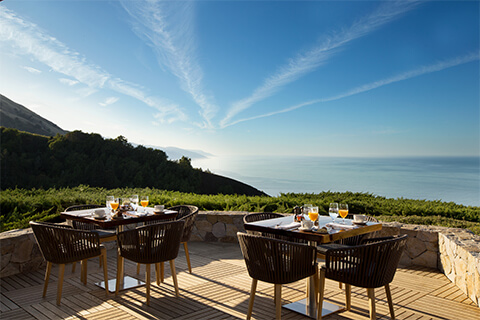 This is an image of a couple of outdoor chairs and tables overlooking the mountains at ocean at The Sur House Restaurant at Alila Ventana Big Sur hotel